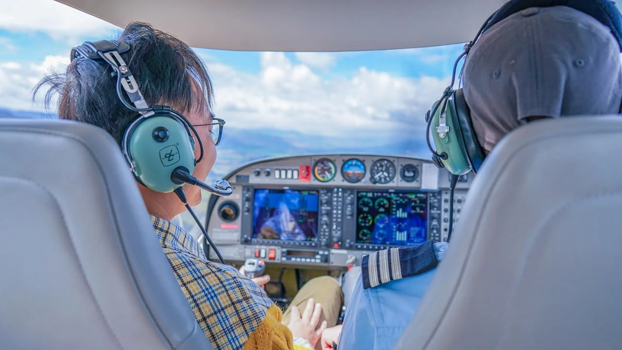 Two people sat in a small aircraft with headphones on, learning how to fly