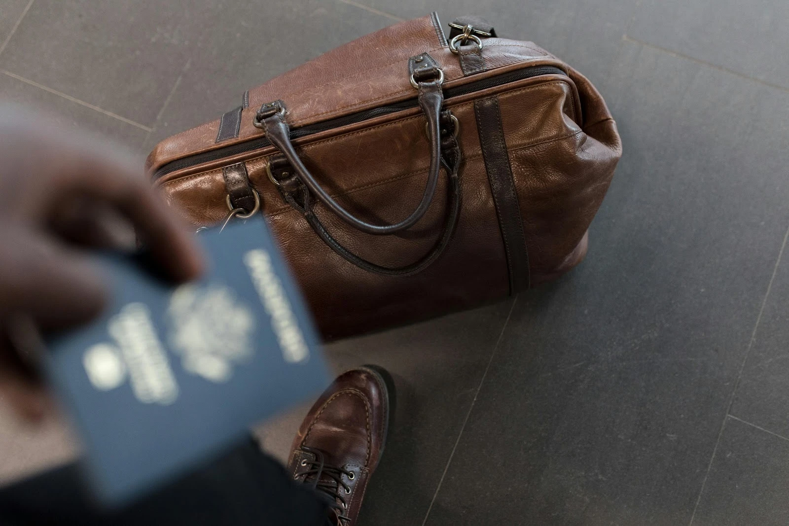 A man holding a passport in his hand with a duffel bag on the floor 