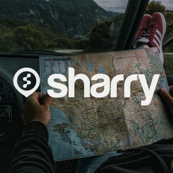 логотип і назва компанії Sharry на фоні чоловіка у червоних кросівках, що сидить в машині та тримає в руках карту