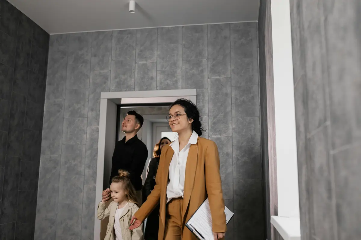 Експерт із планшетом проводить технічний огляд приміщення для родини з дитиною. Вони перевіряють стан стін та якість оздоблення в новобудові. Зображення ілюструє етап пошуку прихованих дефектів та перевірки інженерних систем.