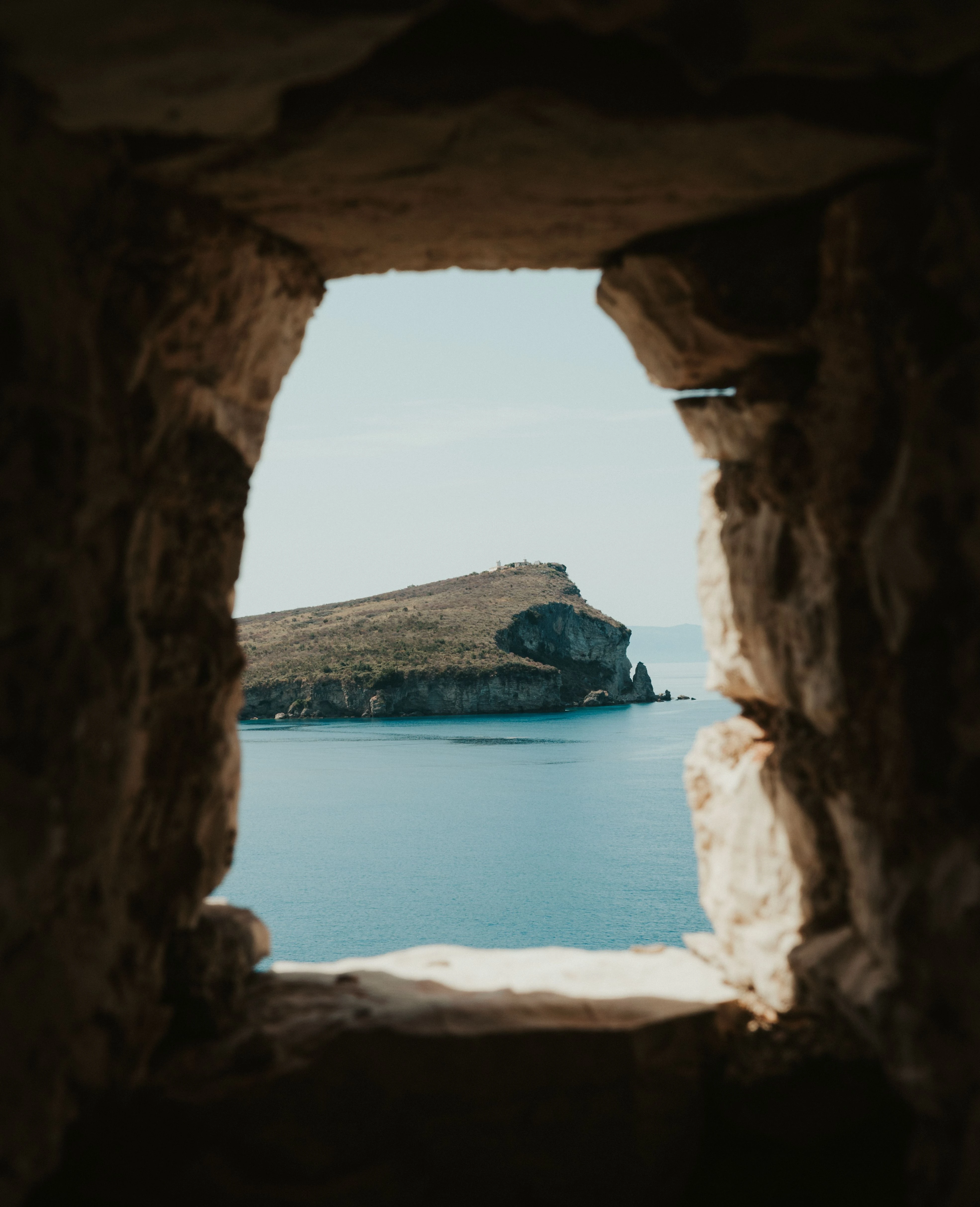 View of the Albanian coast through a rustic stone window in Porto Palermo