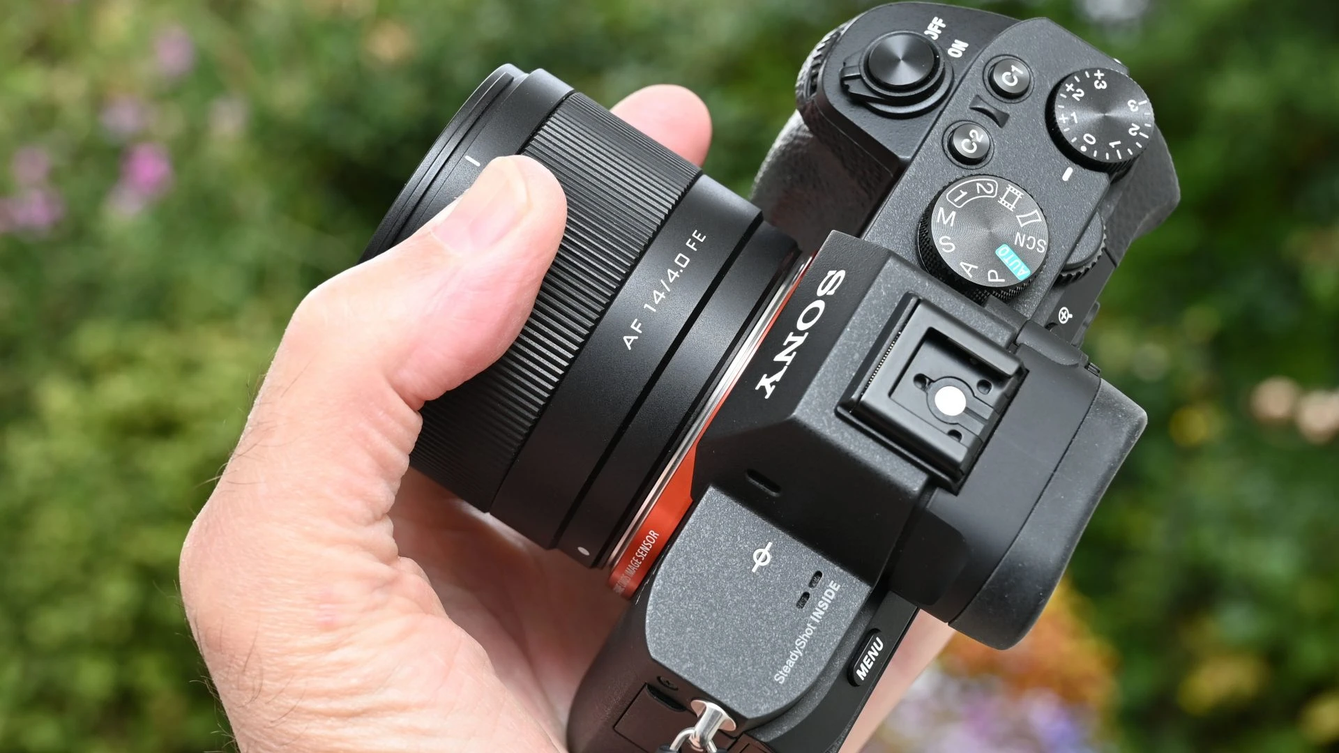 Бездзеркальна тушка Sony A7 з об'єктивом Viltrox AF 14mm f/4.0 Air FE у руці, вид зверху-збоку на металеве кріплення та перемикач режимів камери.
