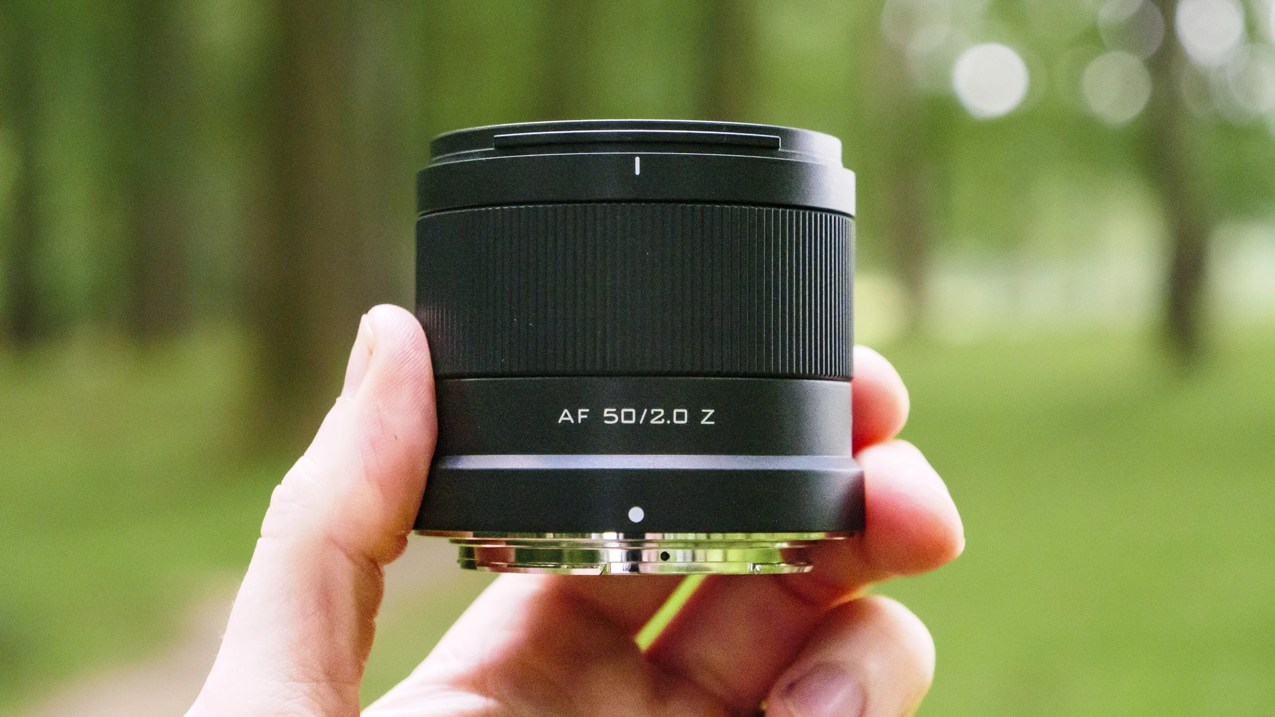 Компактний фікс-об'єктив Viltrox AF 50mm f/2.0 Air у руці на тлі розмитого зеленого парку, демонстрація надмалої ваги корпусу.