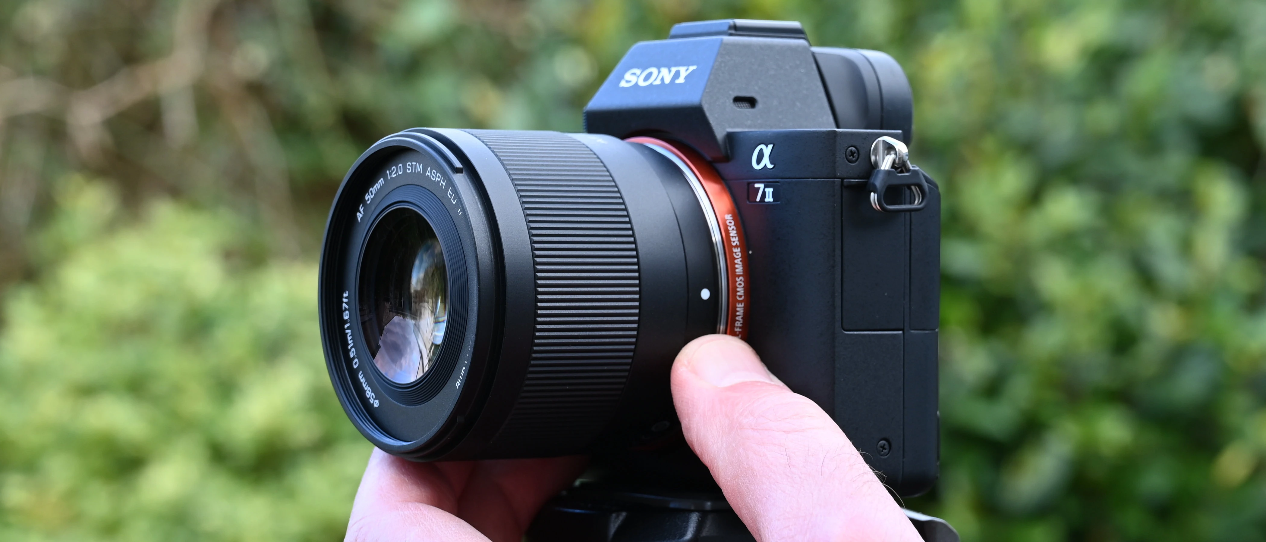 Об'єктив Viltrox AF 50mm f/2.0 Air FE на повнокадровій тушці Sony A7 II у руці, вид на профіль корпусу із металевим кільцем кріплення.
