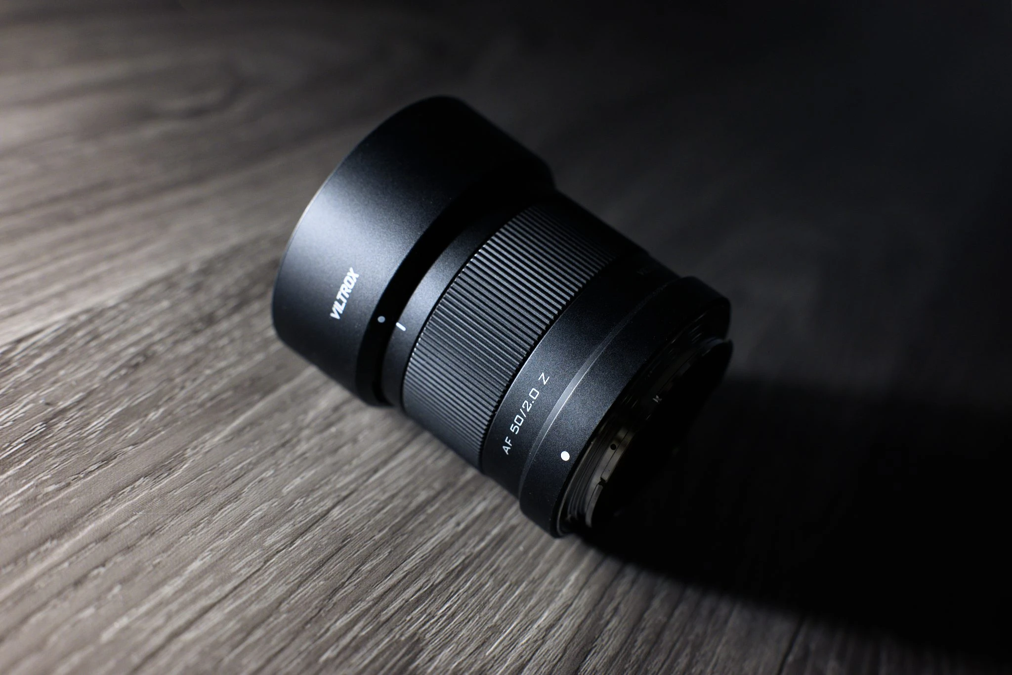 Об'єктив Viltrox AF 50mm f/2.0 Air із встановленою комплектуючою пластиковою блендою на дерев'яному столі в студійному освітленні.
