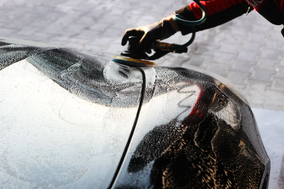 Technician using a dual-action polisher on a black car hood during paint correction