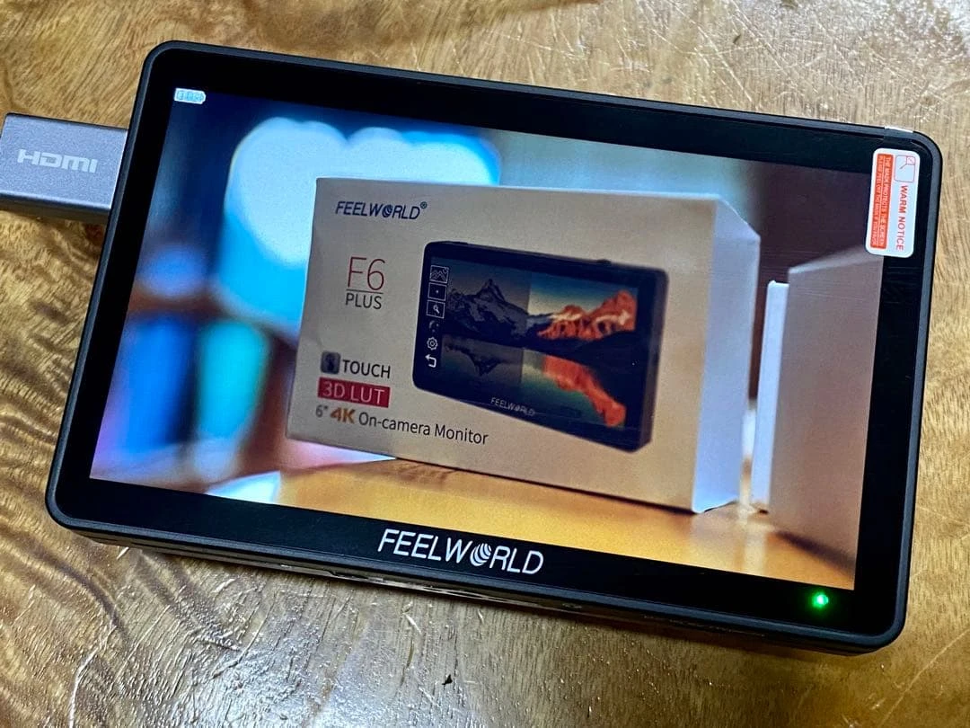Монітор Feelworld F6 Plus V2 на столі з підключеним HDMI кабелем та зображенням коробки на дисплеї