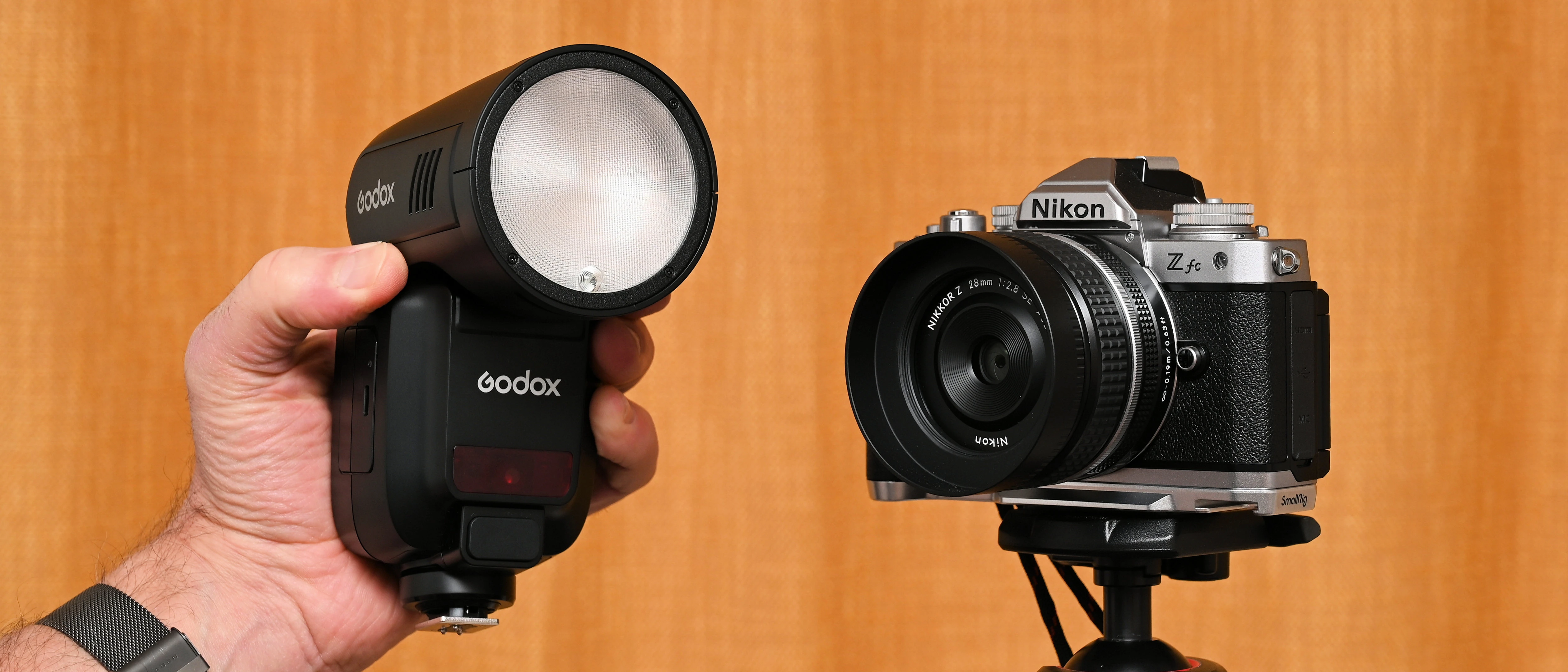 Спалах Godox V100 з круглою матовою лінзою та світлодіодом пілотного світла поруч із камерою Nikon Z fc на штативі