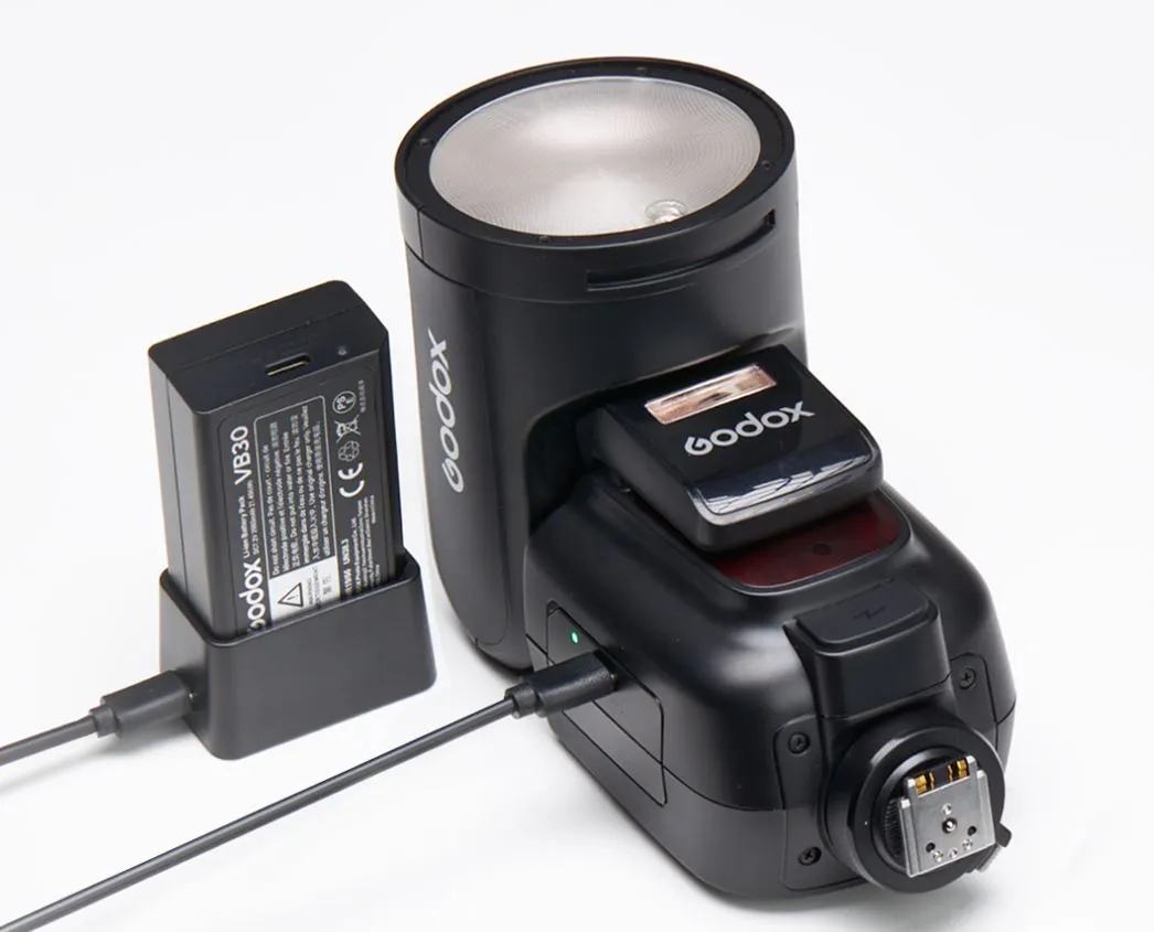 Спалах Godox V1Pro C на зарядці через кабель USB-C поруч із окремим літій-іонним акумулятором VB30 у зарядному кредлі