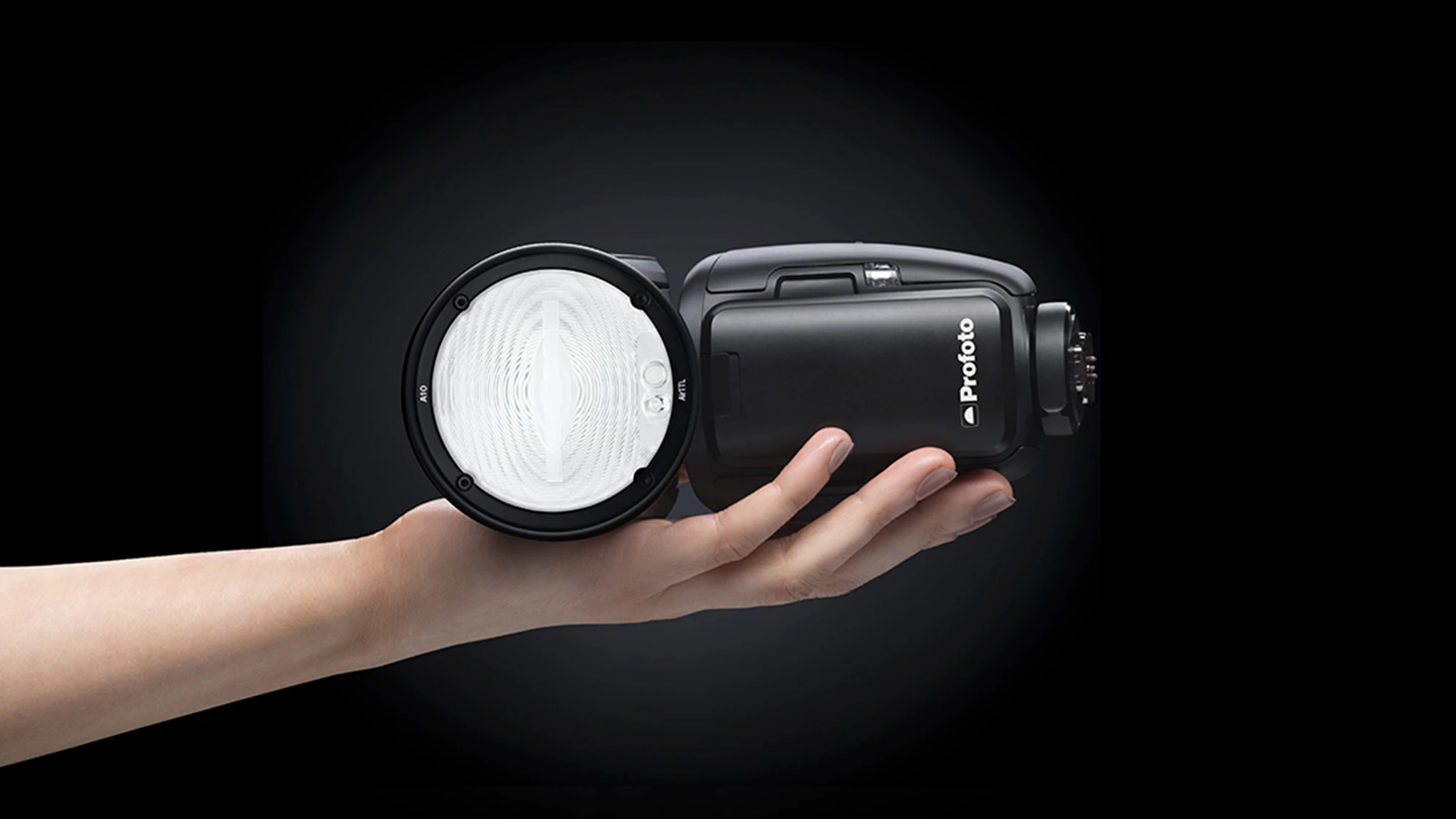 Спалах Profoto A10 на долоні на чорному тлі з маркуванням A10 AirTTL на лінзі та акумулятором спереду