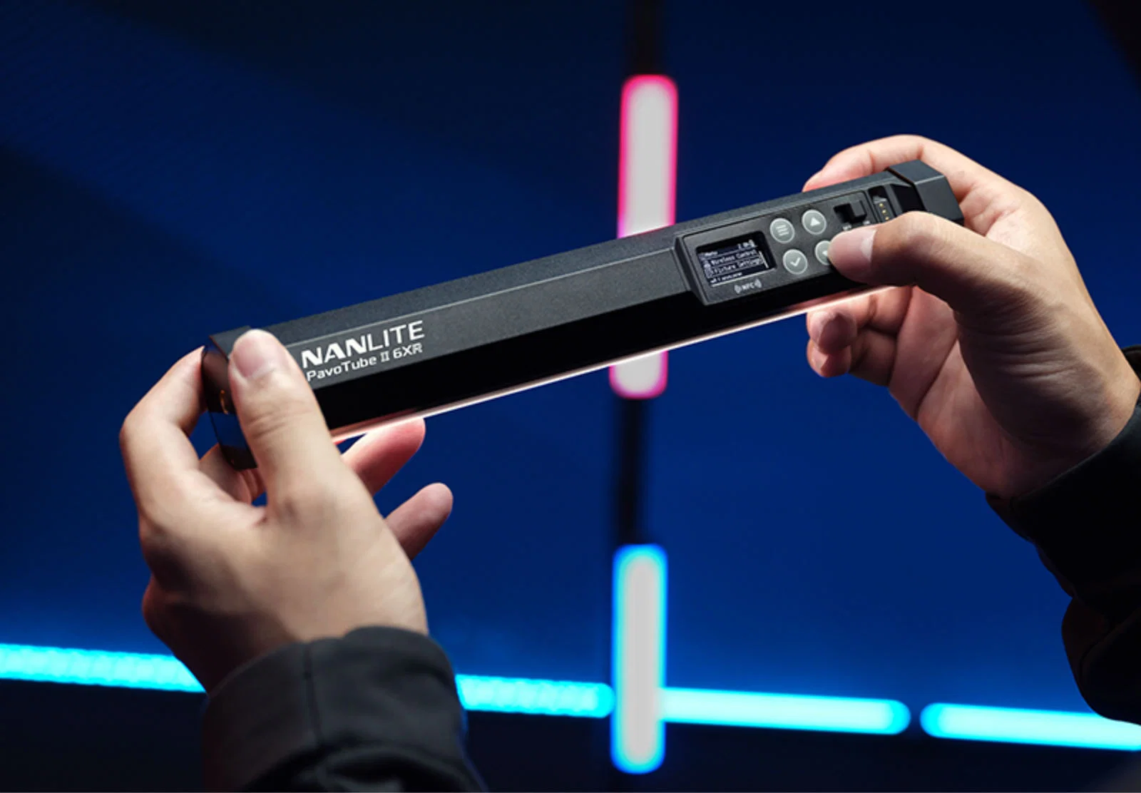 Оператор тримає в руках трубку Nanlite PavoTube II 6XR і пальцем перемикає меню на OLED-екрані поруч із позначкою бездротового модуля NFC