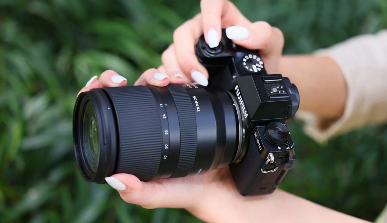 Об'єктив Tamron 17-70mm f/2.8 Di III-A VC RXD у руках фотографа на камері Fujifilm X-S10 на фоні зеленого листя
