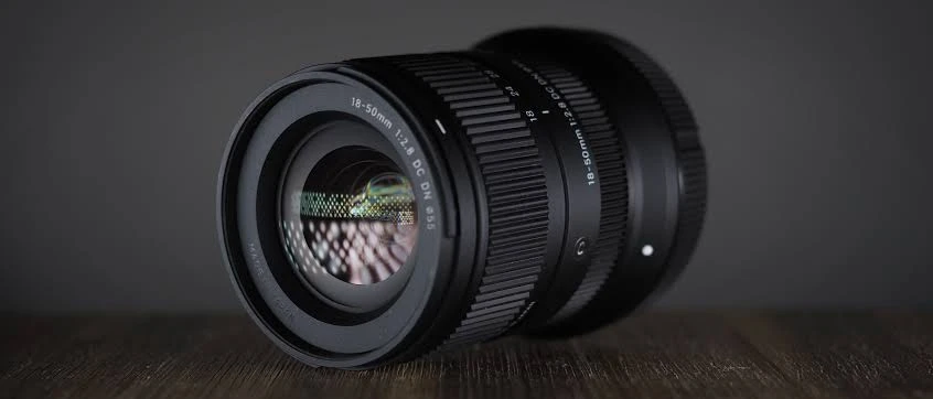 Передня лінза об'єктива Sigma 18-50mm f/2.8 DC DN Contemporary з різьбою під фільтр 55 мм на темному дерев'яному столі