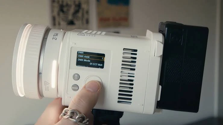 Рука налаштовує меню на моноблоці Godox ML150Bi, до якого позаду через штатний адаптер ML-VMA приєднано акумулятор V-Mount