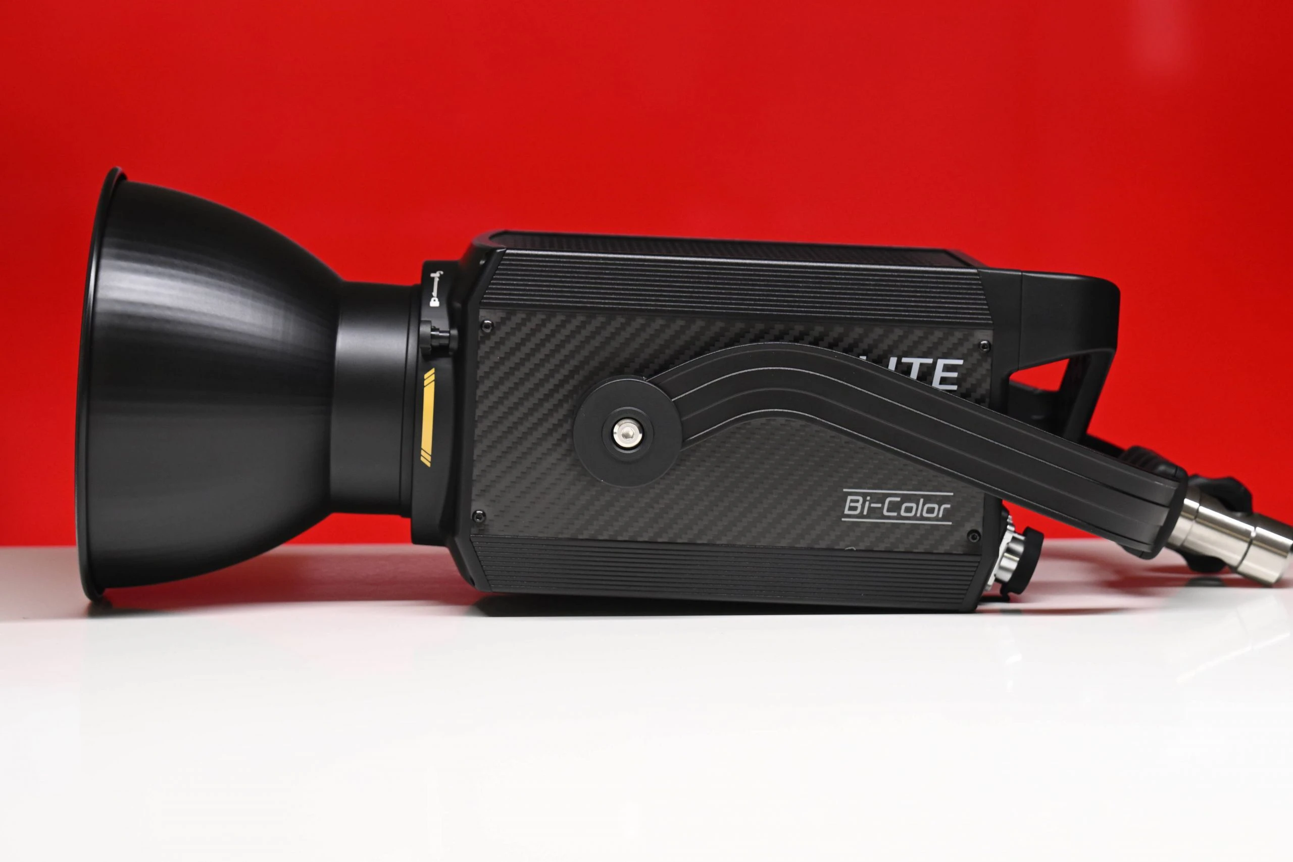 Моноблок Nanlite Forza 500B II з комплектним рефлектором 55 градусів та карбоновою накладкою лежить на столі на червоному тлі