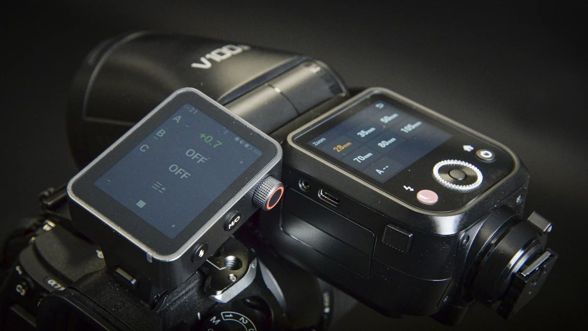 Радіосинхронізатор Godox X3Pro на камері Sony Alpha поруч зі спалахом Godox V100 та акцентом на бічному колісі налаштування на темному тлі