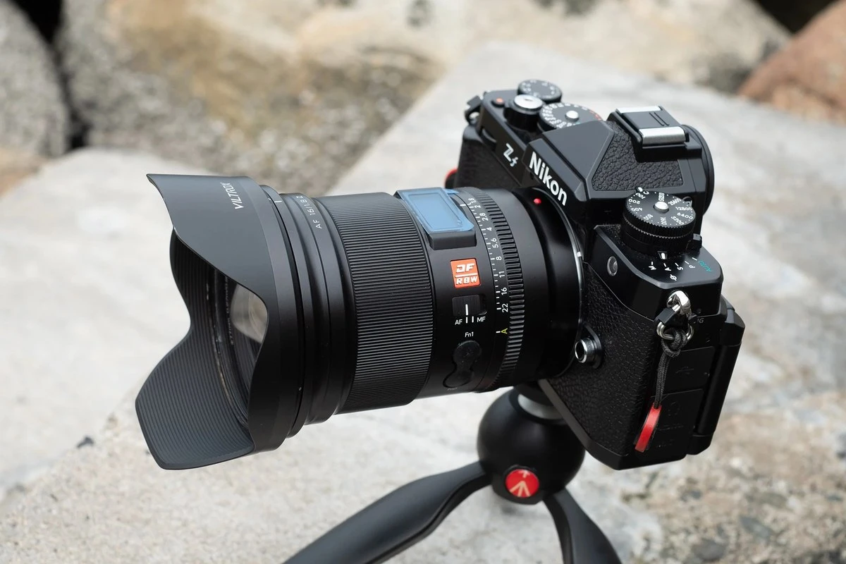 Камера Nikon Z f на міні-штативі з встановленим об'єктивом Viltrox AF 16mm f/1.8 Z та пелюстковою блендою на фоні кам'яних плит