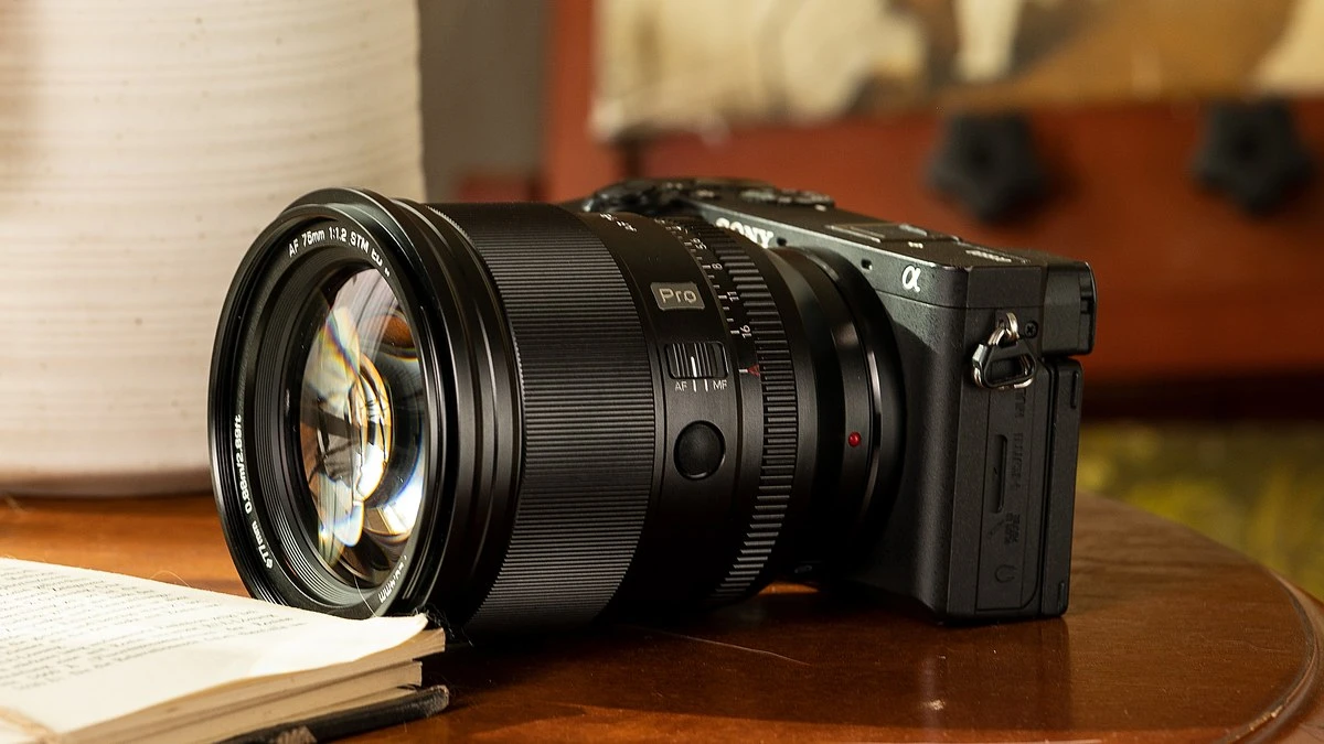 Об'єктив Viltrox AF 75mm f/1.2 Pro на корпусі бездзеркальної камери на полірованому дерев'яному столі поруч із книгою та вазою