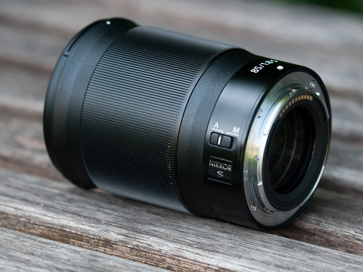 Об'єктив Nikkor Z 85mm f/1.8 S на дерев'яній стільниці на відкритому повітрі з видом на металевий байонет Z-mount та контактну групу