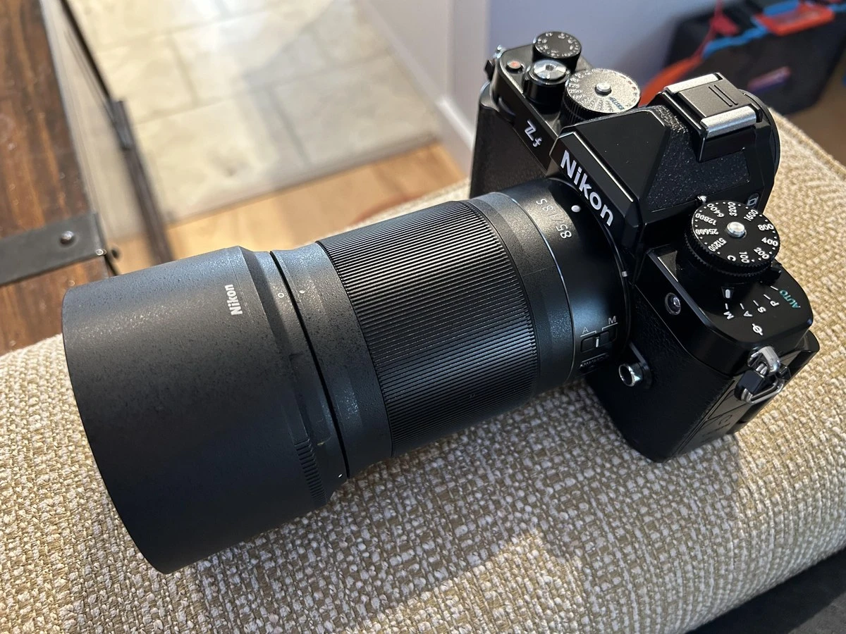 Повнокадрова ретро-камера Nikon Z f з встановленим об'єктивом Nikkor Z 85mm f/1.8 S та масивною циліндричною блендою HB-91 у приміщенні