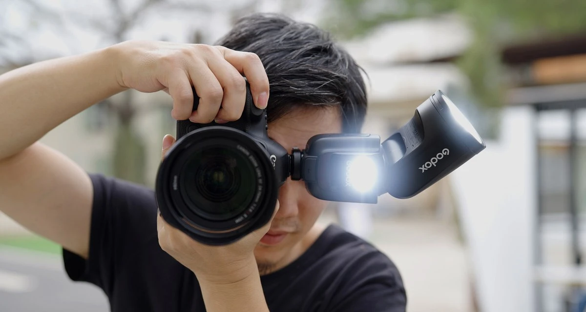 Спалах Godox V1Pro з круглою імпульсною голівкою, встановленим додатковим модулем SU-1 та відкинутим білим відбивачем на нейтральному сірому фоні