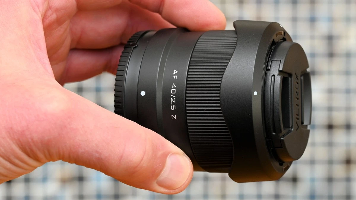 Легкий объектив Viltrox AF 40mm f/2.5 Z в руке с установленной лепестковой блендой и фирменной защитной крышкой.