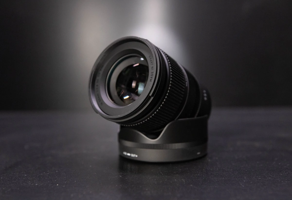 Объектив Sigma 18-50mm F2.8 DC DN лежит под углом на надетой бленде на черном матовом студийном столе