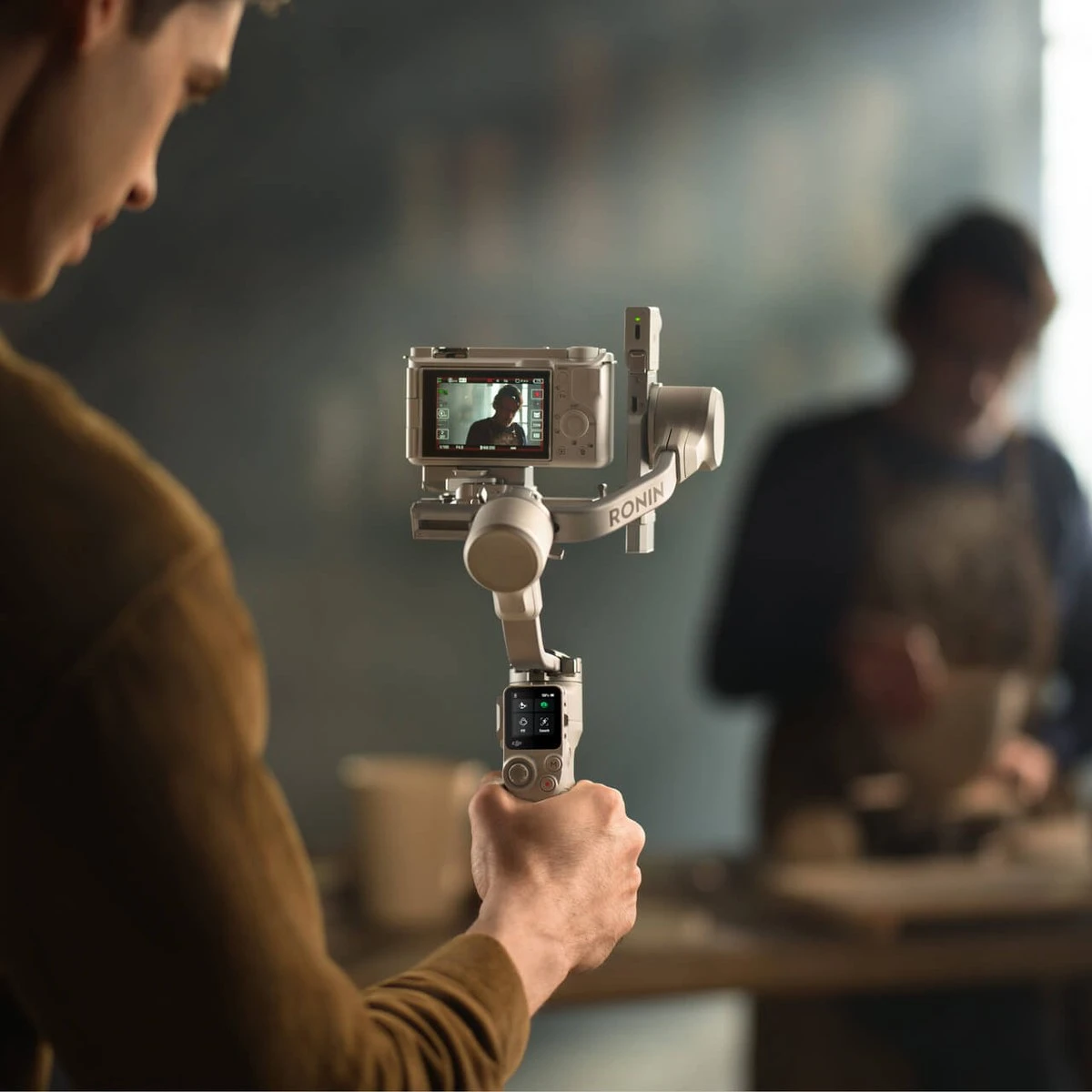 Оператор одной рукой держит стедикам DJI RS 4 Mini с камерой во время съемки гончара за работой в мастерской