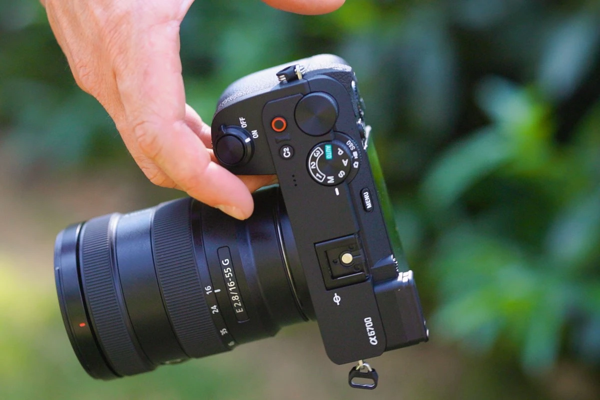 Рука оператора удерживает анатомический хват камеры Sony Alpha 6700 с видимым селектором режимов фото, видео и медленной съемки