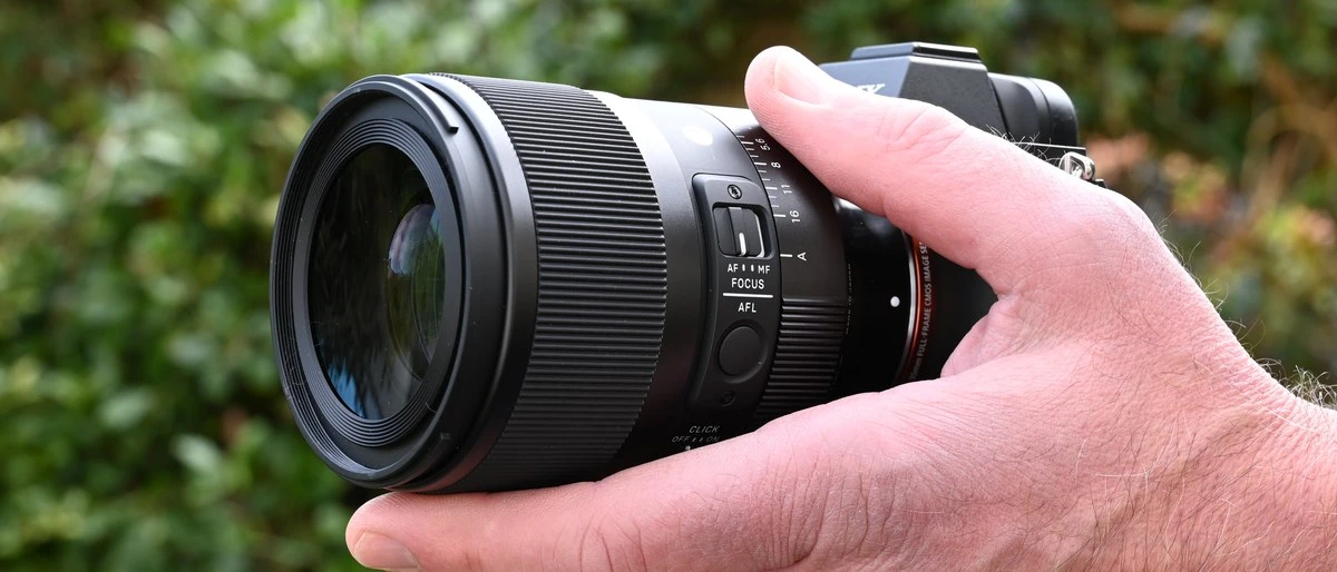 Об'єктив Sigma 50mm f1.2 DG DN Art у руці фотографа на відкритому повітрі на фоні розмитої зелені
