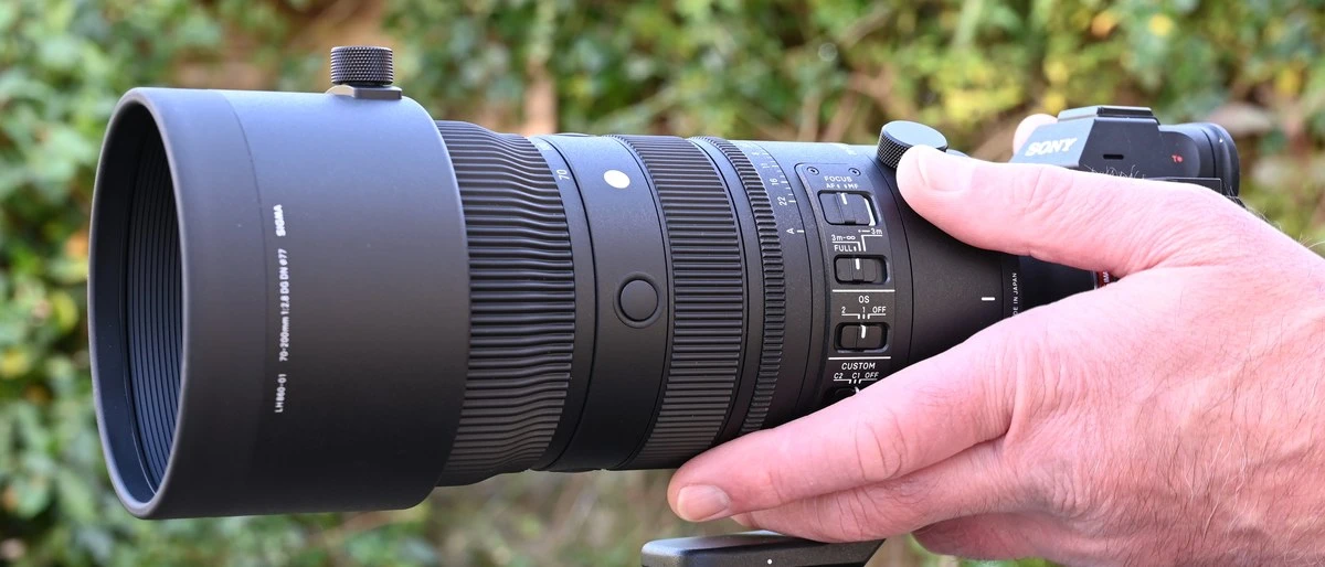 Телеоб'єктив Sigma 70-200mm f2.8 DG DN OS Sports у руках фотографа на відкритому повітрі біля цегляної стіни
