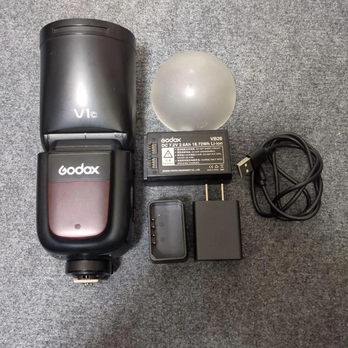 Спалах Godox V1C з круглою головкою, літій-іонним акумулятором VB26, зарядним пристроєм VC26 та розсіювачем AK-R11 Dome на білому студійному тлі