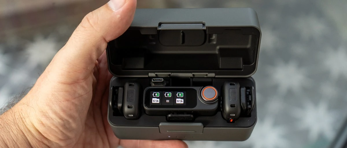 Открытый зарядный кейс радиосистемы DJI Mic 3 с установленными передатчиками и приемником с активным OLED-дисплеем в руке