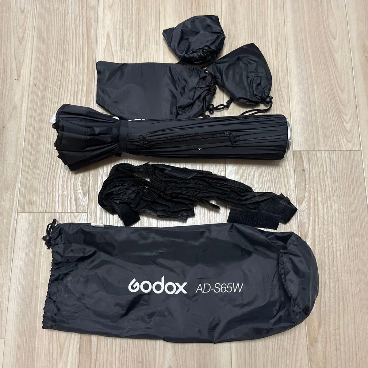 Сложенный софтбокс Godox AD-S65W с сотовой решеткой на липучках, сменными дефлекторами в чехлах и сумкой на деревянном полу