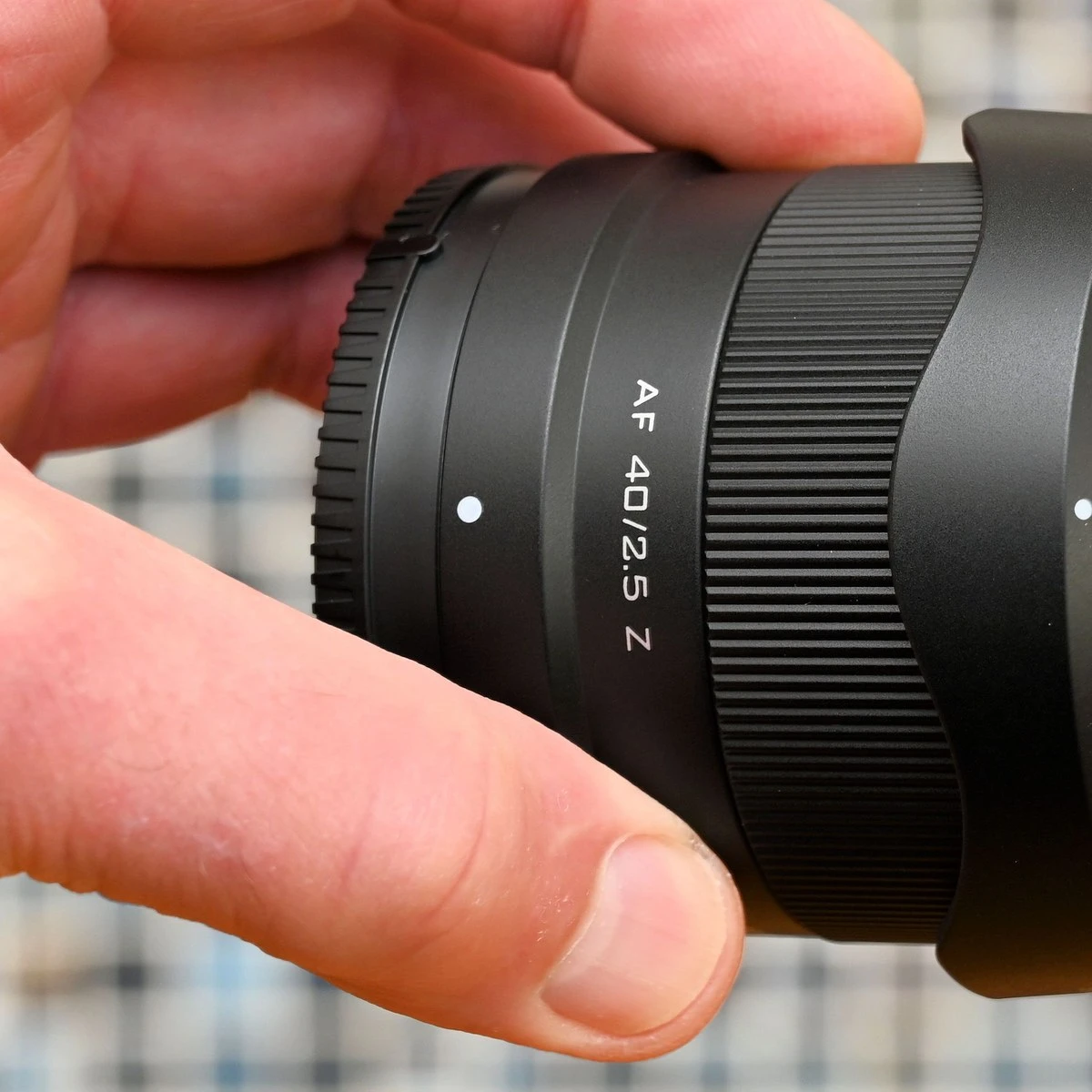 Макроснимок корпуса компактного объектива Viltrox AF 40mm f/2.5 Z в руке на фоне размытой сетчатой текстуры, видно широкое кольцо фокусировки с мелким рифлением