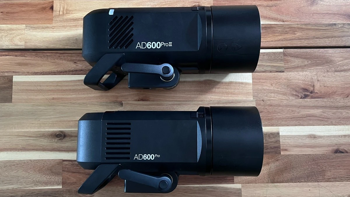 Сравнение двух поколений моноблоков Godox на деревянном столе: AD600Pro II с диагональными вентиляционными прорезями и классический AD600Pro с горизонтальными