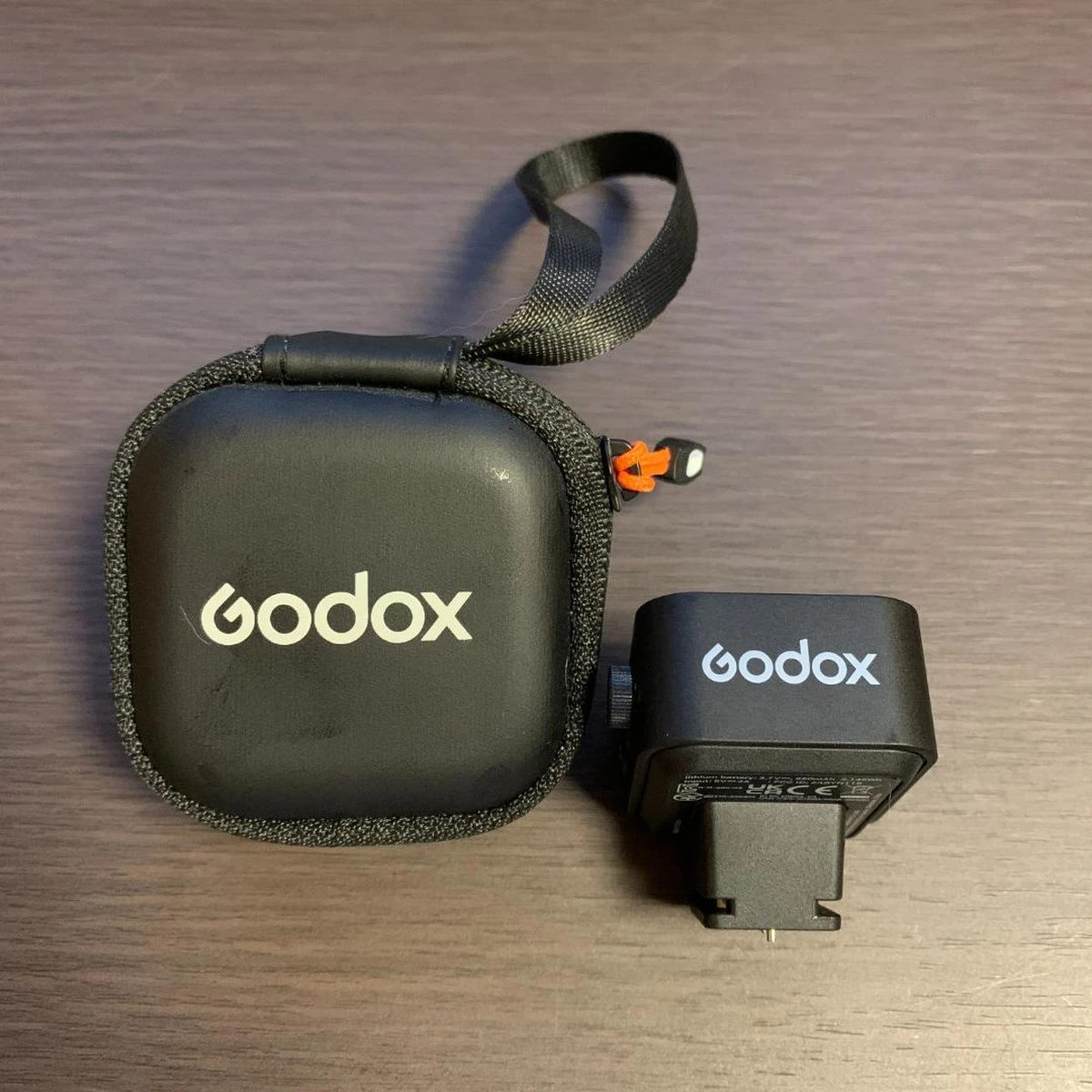 Компактний радіотригер Godox X3 C поруч із фірмовим захисним чохлом на блискавці на дерев'яній поверхні