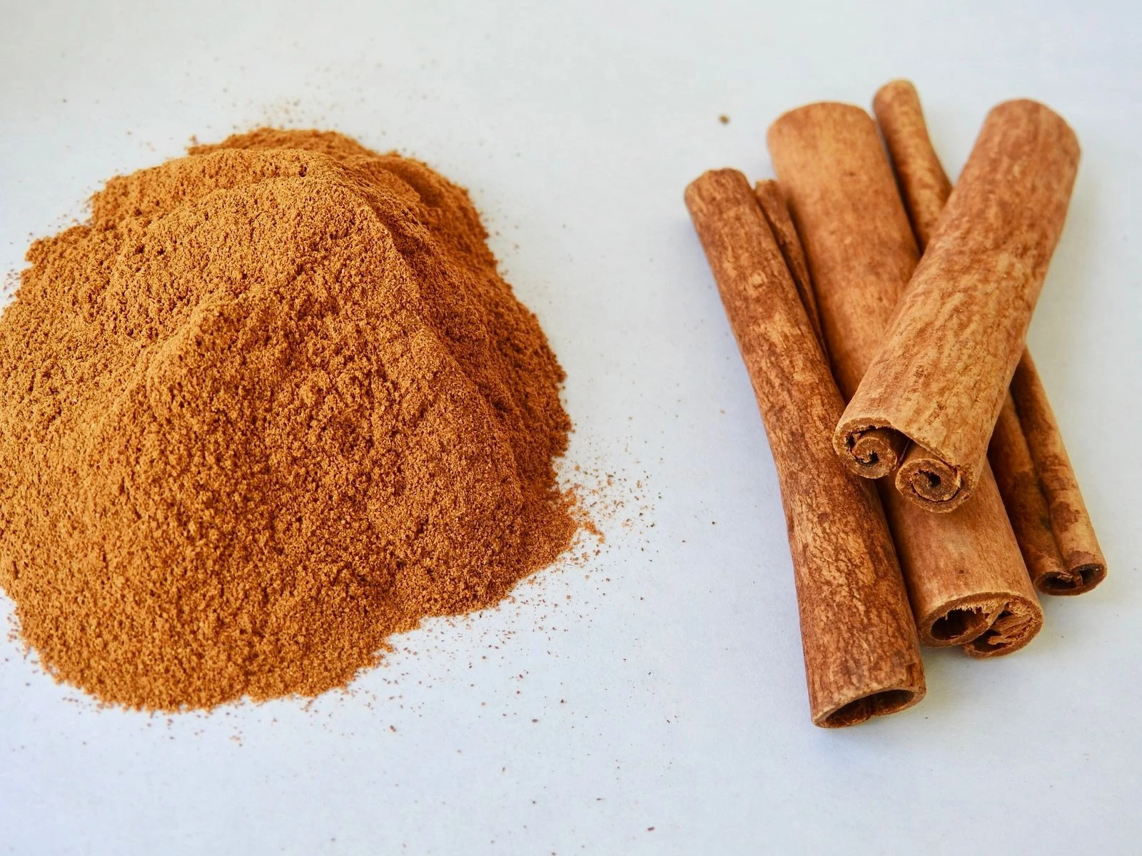 Ground cinnamon beside a bundle of cinnamon sticks on a white surface