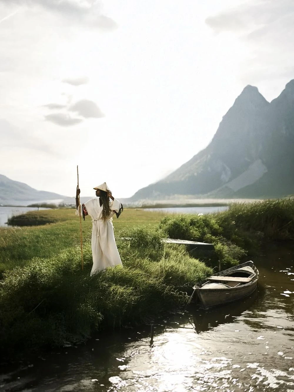 12 Hidden Gems In Valencia For A Different Experience 5 Woman in a white robe and straw hat standing by a traditional wooden boat on the edge of the Albufera lagoon