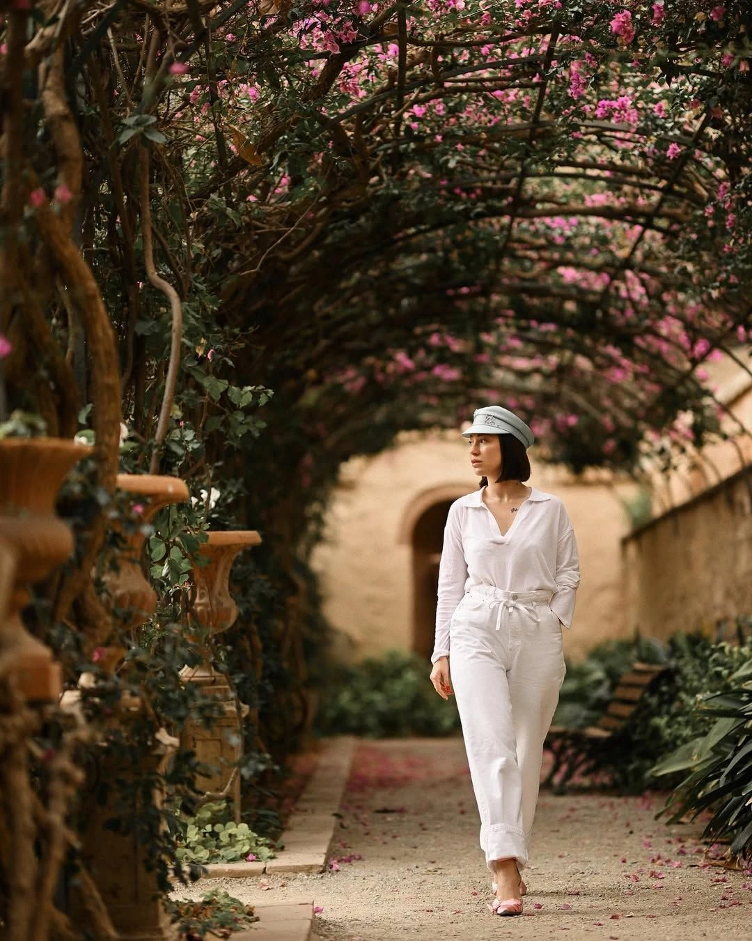 12 Hidden Gems In Valencia For A Different Experience 4 Woman in white walking under an arch of pink bougainvillea in a quiet garden in Valencia