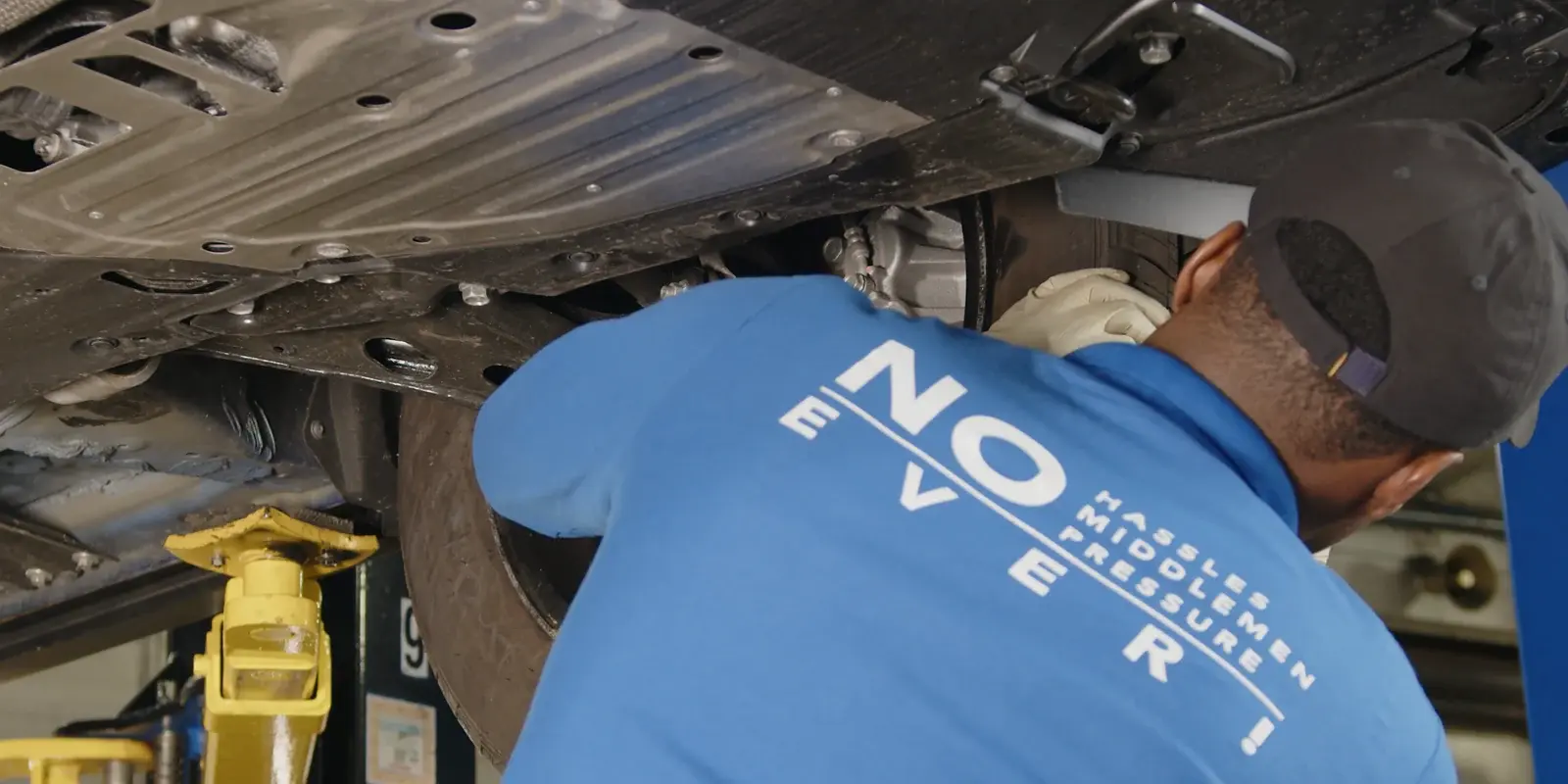 Technician inspecting the underbody and wheel area of a vehicle raised on a lift in a service bay