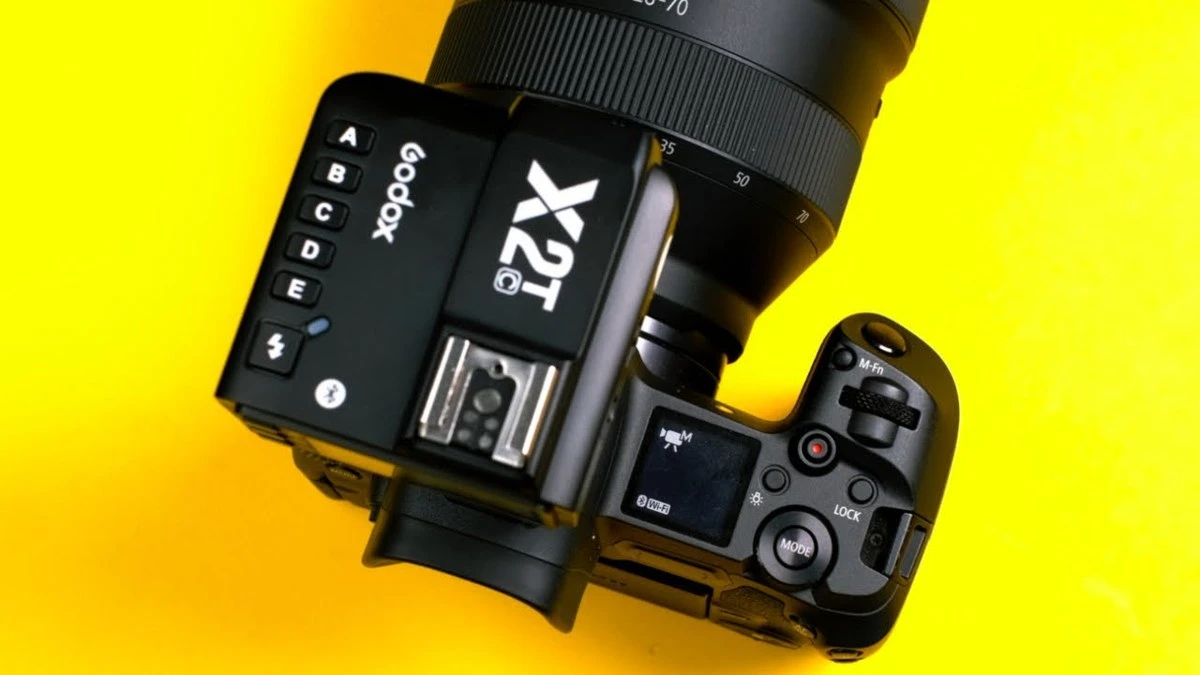 Радіосинхронізатор Godox X2T-C з верхнім наскрізним гарячим башмаком встановлений на камеру Canon зверху на яскраво-жовтому фоні