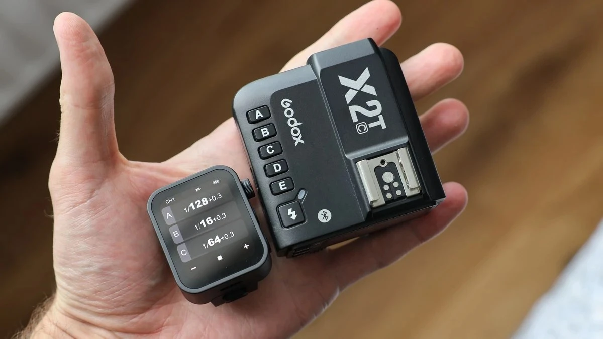Долоня оператора тримає синхронізатор Godox X2T-C з фізичними кнопками поруч з компактним сенсорним тригером Godox X3