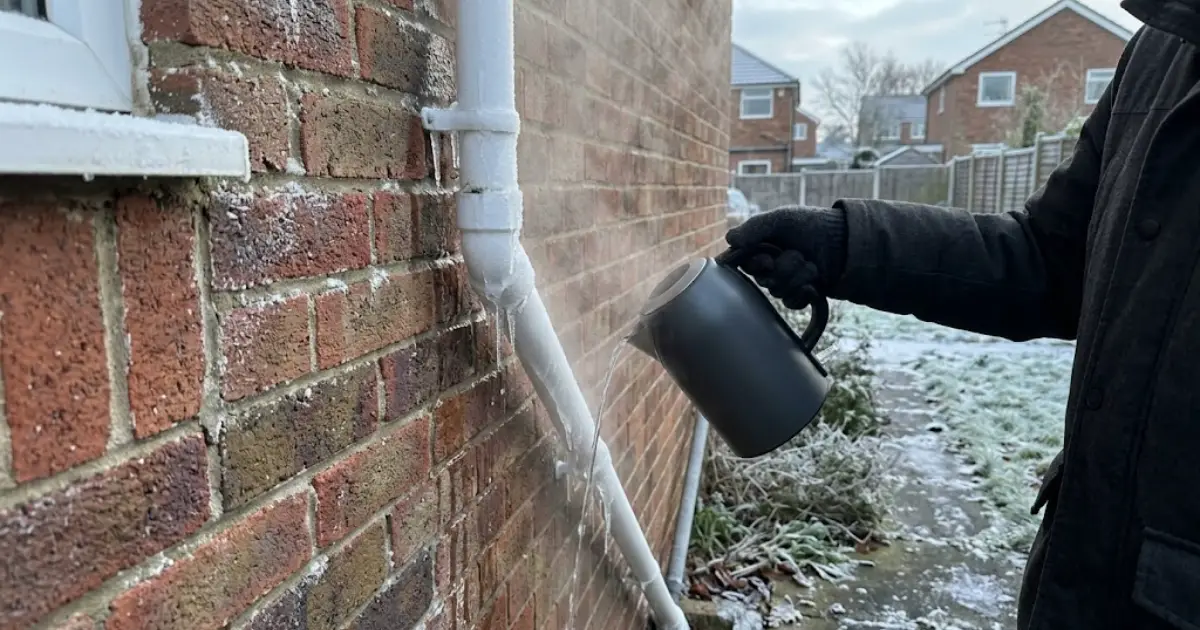 Frozen condensate pipe on a UK brick house being thawed with warm water from a kettle