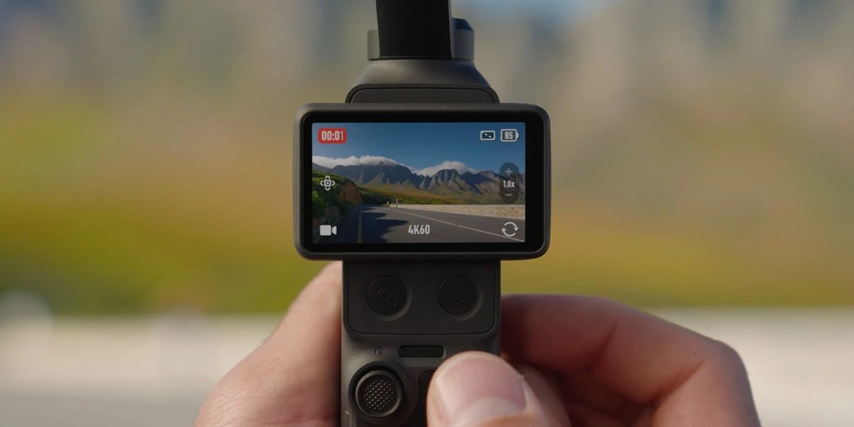 Камера DJI Osmo Pocket 4 у руці з розвернутим горизонтальним поворотним екраном, де відображається режим 4K60 та заряд 85%
