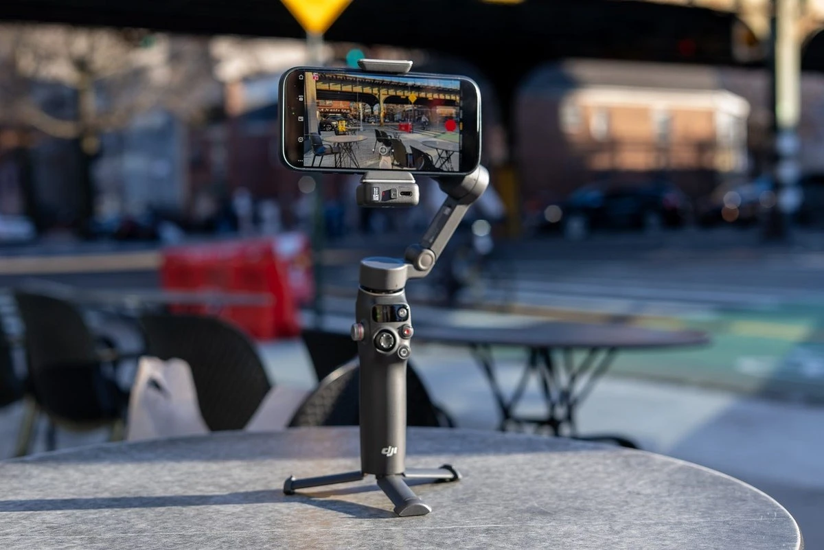 Стабилизатор DJI Osmo Mobile 7P со смартфоном в магнитном зажиме стоит на столе на встроенной ножке